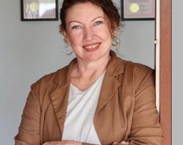 Professional headshot of smiling hypnotherapist Marisa with framed qualifications in background