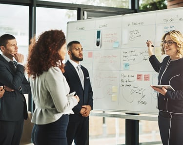 Diverse business team collaborating on project management using a whiteboard in a modern office.