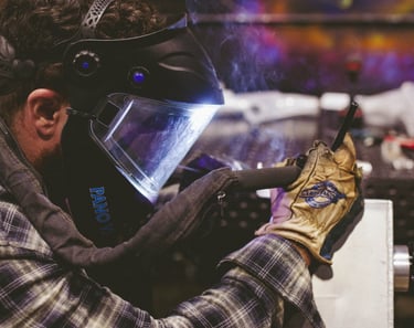 Professional welder wearing a protective mask and gloves while welding metal at Stronghand Tools.