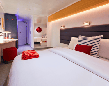 Modern cruise ship cabin featuring a plush bed with nautical striped pillows and a vanity desk.
