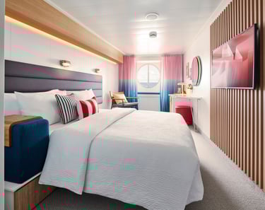 Modern cruise ship cabin with a king-size bed, porthole window, and contemporary decor.