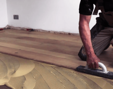 Professional installer installing hardwood flooring using glue down method.