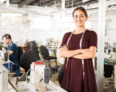 Una diseñadora de moda sonriente de pie en una fábrica de ropa con máquinas de coser
