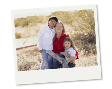 A grandmother smiling with her two young grandchildren in a sunny outdoor desert setting.