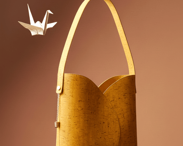 Eco-friendly yellow cork leather shoulder bag floating next to a white origami crane.