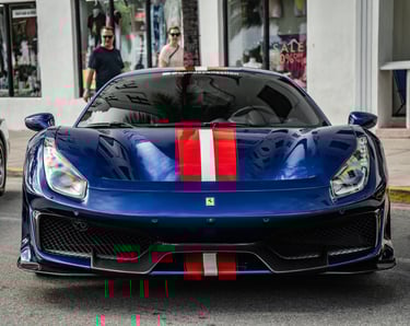 A blue Ferrari 488 Pista luxury supercar with red and white racing stripes parked on a city street.