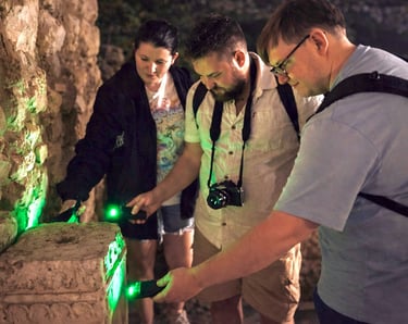 Tour participants examining ancient stone ruins with green UV lights during Athens Ghost Tour