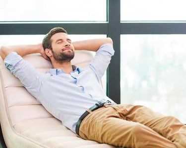 A relaxed man leaning back on a lounge chair with eyes closed, enjoying a break in a modern office.