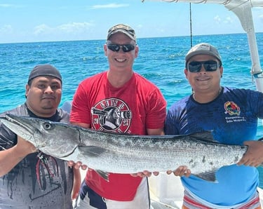 Smiling fishermen holding a large barracuda on a deep sea fishing charter boat in tropical blue waters.