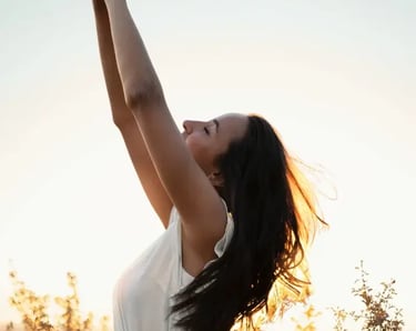 Une femme en robe blanche dans un champ lève les bras vers le ciel, exprimant légèreté et liberté.