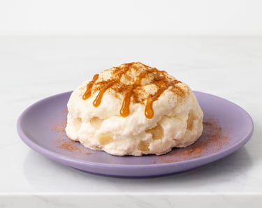 A high protein, creamy dessert pudding topped with caramel sauce and cinnamon on a purple plate.