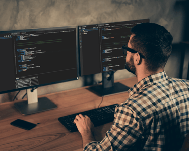 A man sitting at a desk with two monitors and a keyboard writing code