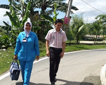 A healthcare nurse and doctor walk along a village road for a community home visit.