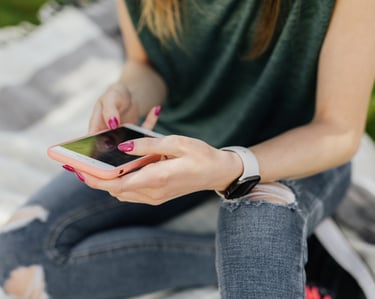 A teenage girl wearing ripped jeans sitting on a blanket looking at her phone
