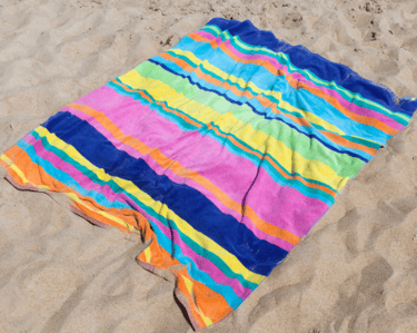 A brightly coloured striped towel lies on sand