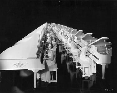 Regimented rows of white grand pianos played by chorus girls in white costumes, forming an endless l