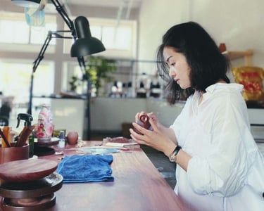 Artisan seated at a workbench, holding a Zisha teapot and examining it closely