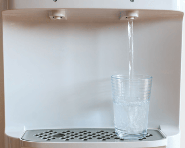 a glass of water is being poured into a water dispenser