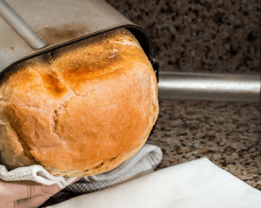 a person holding a loafed bread in a kitchen