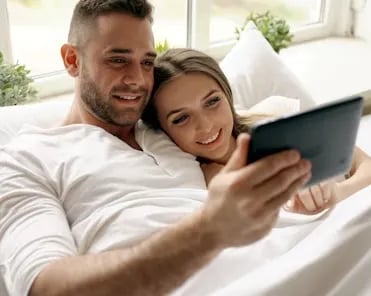 Couple watching tablet in bed for bible answers