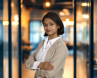Professional businesswoman in a beige blazer standing with arms crossed in a modern office.