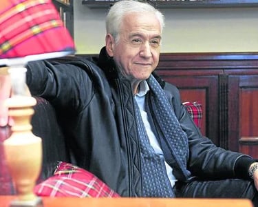 a man in a black jacket and tie dye on a chair