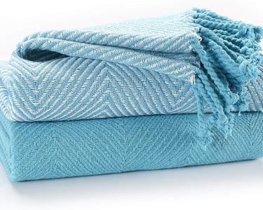 Stacked turquoise cotton throw blankets with white herringbone pattern and fringed edges.