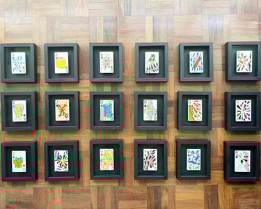 vista de cima das 18 cartas de baralho personalizadas e colecionáveis da série, emolduradas em preto sobre chão de taco.