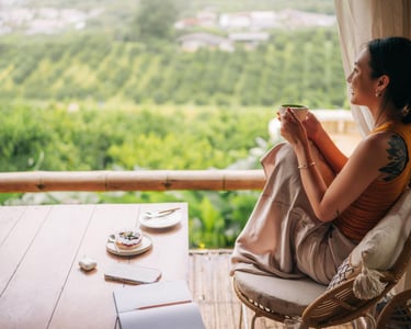 Smiling woman drinking matcha tea on a balcony overlooking a lush green valley at a mountain resort.