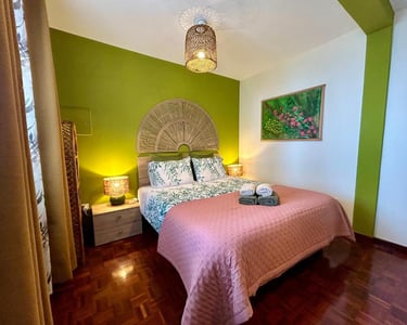 Tropical bedroom interior featuring a green accent wall, rattan headboard, and pink bedspread.
