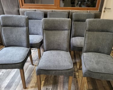 Set of grey upholstered dining chairs with high backs and wooden legs on a rustic laminate floor.