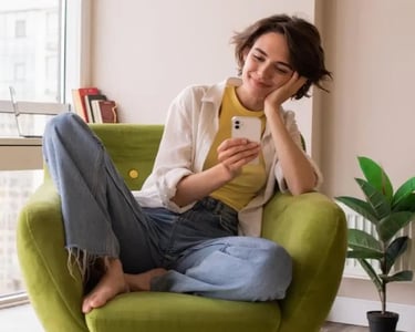 Femme assise confortablement en tailleur, tenant son téléphone et souriant doucement.
