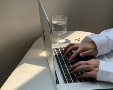 Hands typing on a laptop next to a glass of water in a minimal workspace.
