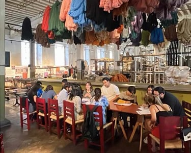 Estudiantes de inglés en un taller textil, sentados alrededor de una gran mesa.