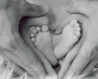 Mãos de mãe e pai segurando os pés de um bebê em formato de coração, simbolizando amor e proteção.