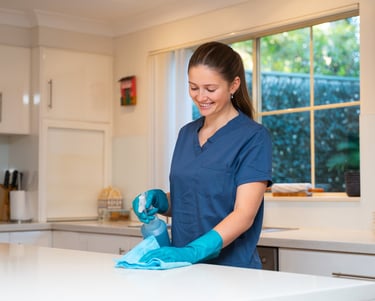 a woman in scrubs and gloves is smiling and cleaning a kitchen counter top