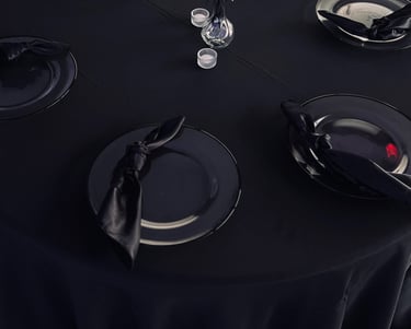 Table ronde élégante pour avec une nappe noire, des assiettes de présentation, des serviettes.