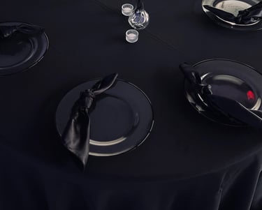 Table ronde élégante pour avec une nappe noire, des assiettes de présentation, des serviettes.