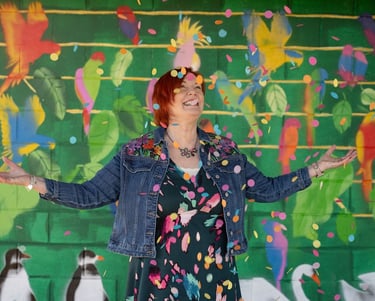 Lady stood in front of a colourful background smiling throwing confetti into the air.