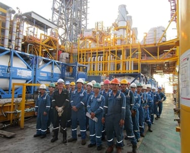 A group of industrial engineers and workers in blue jumpsuits posing at an offshore oil and gas platform.