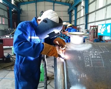 Professional welder in protective gear welding a large industrial steel pipe in a fabrication workshop.