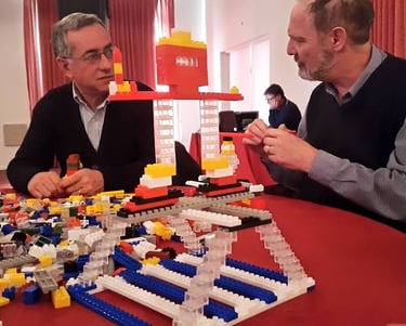 a man and woman sitting at a table with legos Taller Corporasti