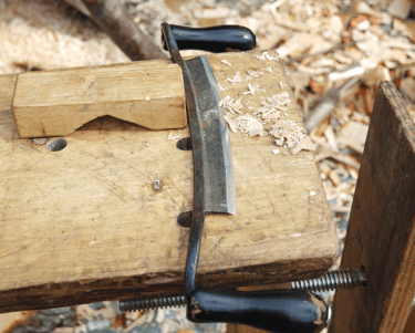 a drawknife with shavings on a piece of timber