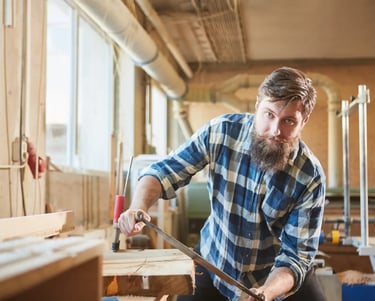 a man in a checked shirt is holding a drawknife and working on timber