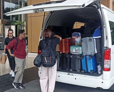 Satu orang pria dua orang wanita sedang menurunkan bagasi dari Hiace.