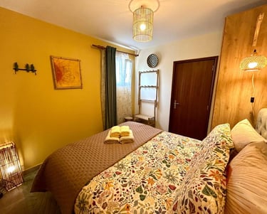 Cozy bedroom interior with a yellow accent wall, floral bedding, and warm bamboo lighting.