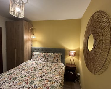 Cozy bedroom with floral bedding, woven wall mirror, and warm ambient lighting from bedside lamps.