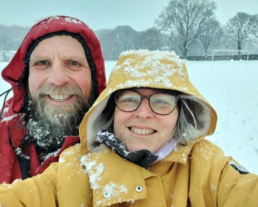 A man with a beard in a red coat and a woman with glasses in a yellow coat in the snow