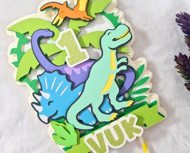 Colorful paper cake topper featuring a cartoon dinosaurs theme with the number "1" at the center. Th