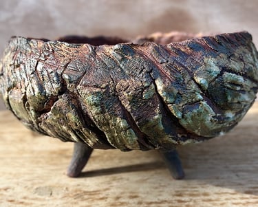 A large ceramic plant pot with 4 conic legs glazed in green and brown with wooden like texture